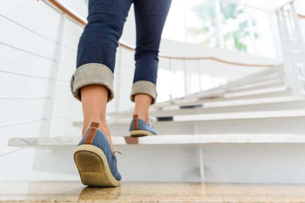 Young adult woman walking up the stairs with sun sport background.